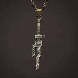 Può includere: Una collana con un ciondolo a forma di spada d'argento con un design dettagliato. Il ciondolo è attaccato a una catena d'oro.