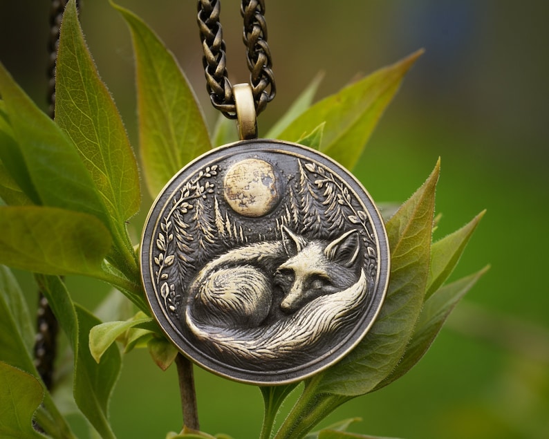 May include: A bronze pendant necklace featuring a detailed depiction of a fox curled up under a full moon in a forest setting.