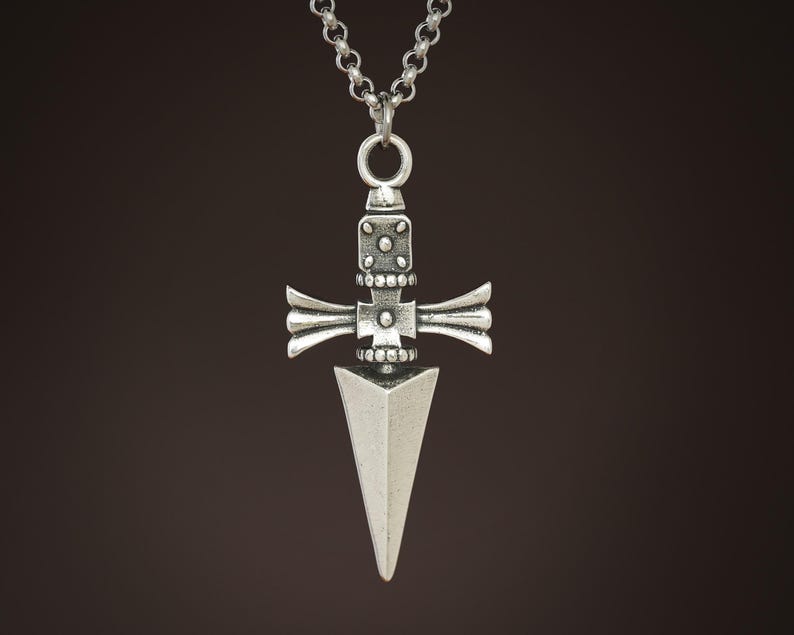 Pu&ograve; includere: Una collana con un ciondolo in argento che presenta un designo a forma di pugnale dettagliato con un manico a forma di croce. Il ciondolo &egrave; sospeso da una catena in argento.