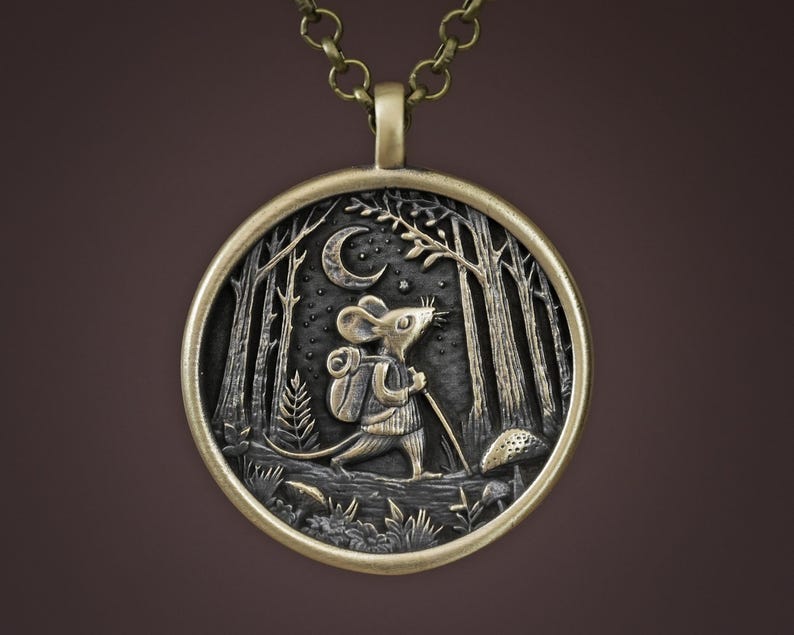 May include: A bronze pendant necklace featuring a detailed, three-dimensional design of a mouse carrying a backpack and walking through a forest under a crescent moon.