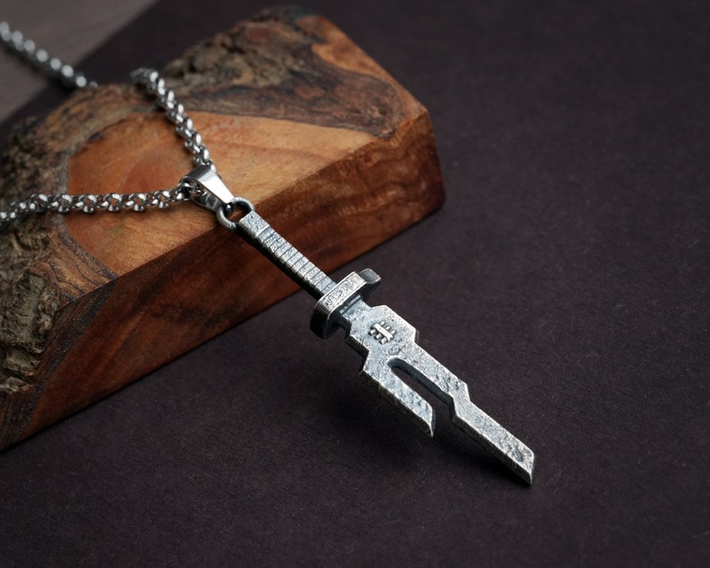 May include: A silver sword pendant necklace with a detailed design. The pendant is attached to a silver chain.