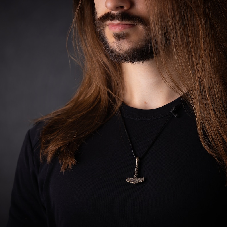 May include: A person with long brown hair wearing a black t-shirt with a silver Mjolnir pendant necklace.