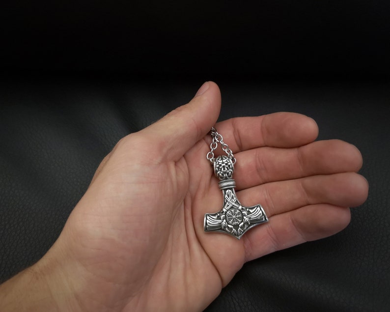 K&ouml;nnte beinhalten: Eine silberne Mjolnir-Halskette mit filigranen Details. Der Anh&auml;nger hat ein kreisf&ouml;rmiges Design mit einem zentralen Stern und ist an einer silbernen Kette befestigt.