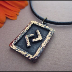 Può includere: Una collana con cordoncino in pelle nera con un ciondolo quadrato che presenta un simbolo a doppio zig-zag dorato.
