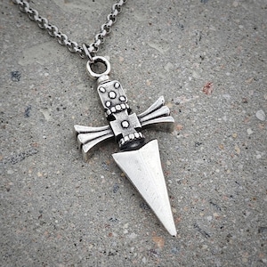 Pu&ograve; includere: Una collana con un ciondolo in argento che presenta un design a pugnale dettagliato con un manico a forma di croce.