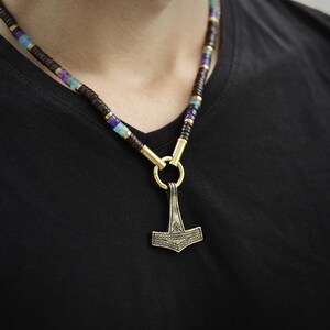 May include: A necklace with a silver Mjolnir pendant and a multi-colored beaded chain. The beads are brown, purple, blue, and green.