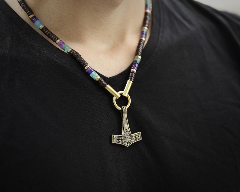 May include: A necklace with a silver Mjolnir pendant and a multi-colored beaded chain. The beads are brown, purple, blue, and green.