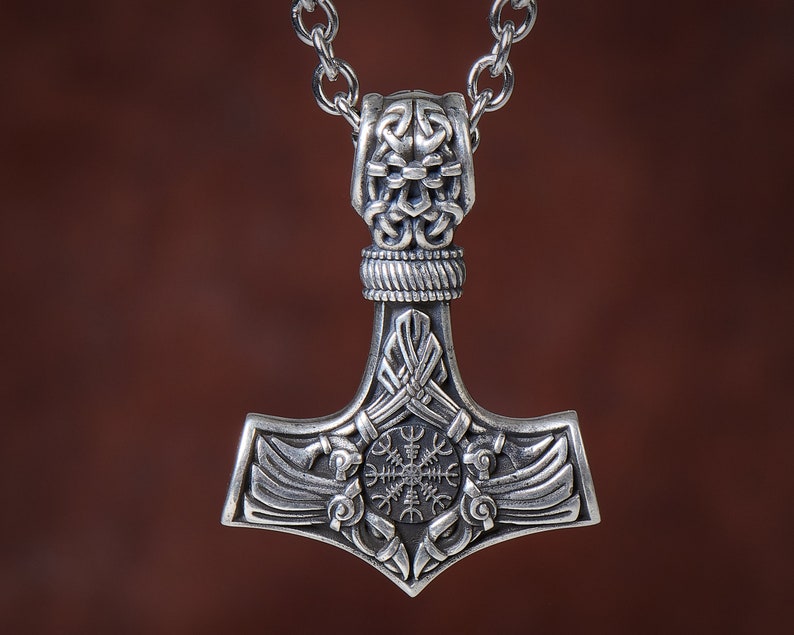 Viking thor hammer pendant showcasing two ravens alongside the Vegvisir, a Viking compass for guidance, and the Aegishjalmur, symbolizing protection. The ravens, intricately detailed, flank the symbols, crafted in silver or bronze