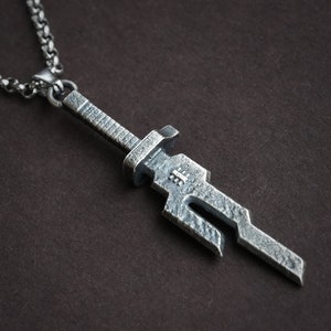 May include: A silver sword pendant necklace with a detailed, textured design. The pendant is attached to a silver chain.