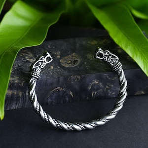 Puede incluir: Una pulsera de plata con un diseño de cuerda trenzada y detalles de cabeza de lobo.