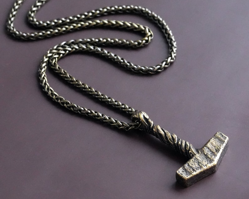 May include: A silver chain necklace with a detailed silver hammer pendant. The chain is a braided style.