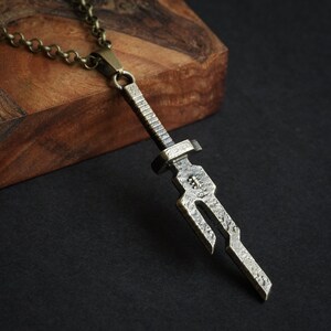May include: A silver-toned sword pendant necklace with a chain. The sword pendant has a detailed, textured design.