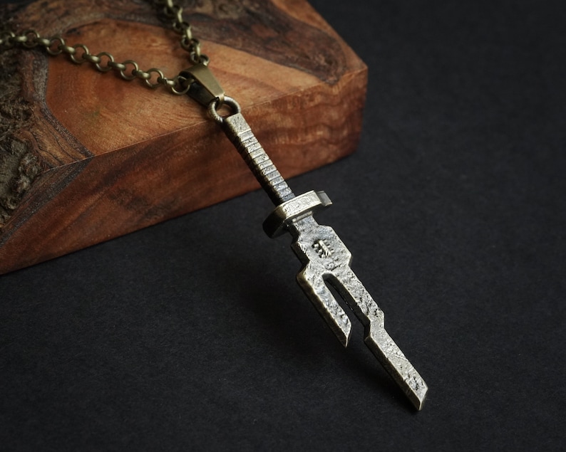 May include: A silver-toned sword pendant necklace with a chain. The sword pendant has a detailed, textured design.