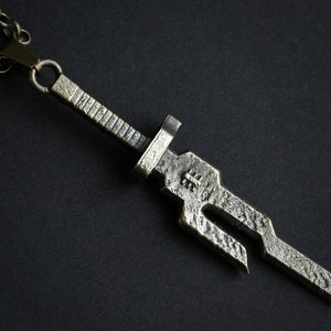May include: A silver-toned sword pendant necklace with a chain. The sword has a textured surface and a detailed design.