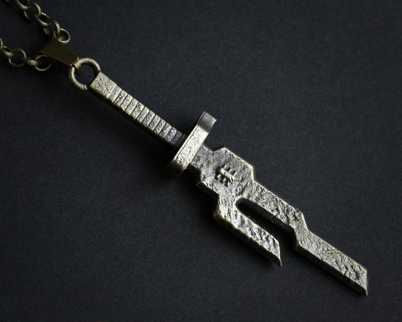 May include: A silver-toned sword pendant necklace with a chain. The sword has a textured surface and a detailed design.