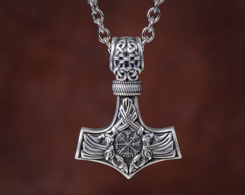 Viking thor hammer pendant showcasing two ravens alongside the Vegvisir, a Viking compass for guidance, and the Aegishjalmur, symbolizing protection. The ravens, intricately detailed, flank the symbols, crafted in silver or bronze