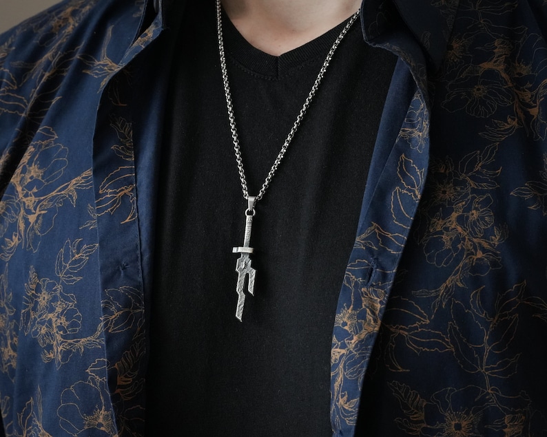 May include: A silver chain necklace with a sword pendant. The pendant is detailed and has a textured finish.