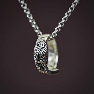 May include: A silver chain necklace with a detailed, ornate pendant in the shape of a ring. The pendant has a floral design.