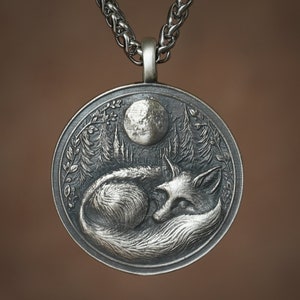 May include: A silver pendant necklace featuring a detailed, three-dimensional design of a fox sleeping under a full moon in a forest setting.