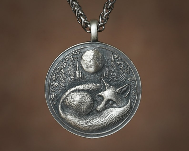 May include: A silver pendant necklace featuring a detailed, three-dimensional design of a fox sleeping under a full moon in a forest setting.