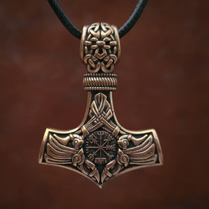 Viking thor hammer pendant showcasing two ravens alongside the Vegvisir, a Viking compass for guidance, and the Aegishjalmur, symbolizing protection. The ravens, intricately detailed, flank the symbols, crafted in silver or bronze