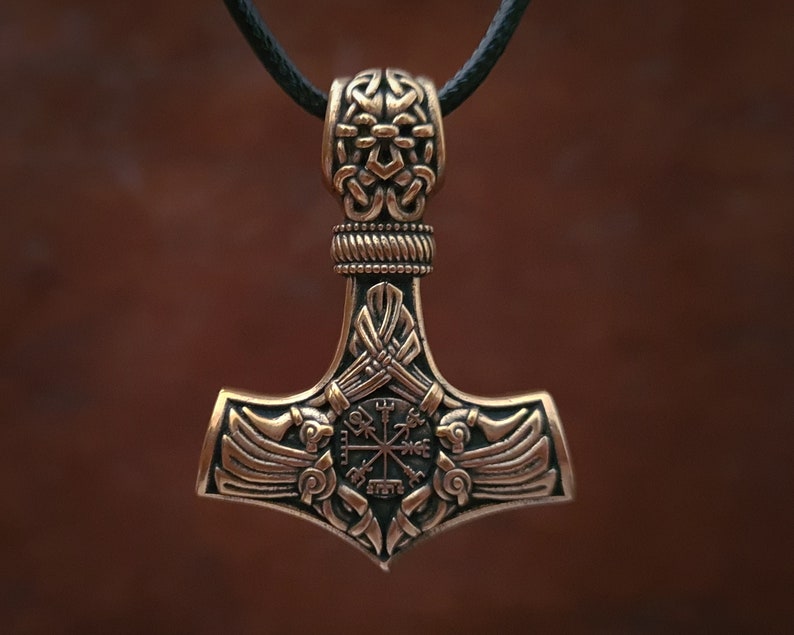 Viking thor hammer pendant showcasing two ravens alongside the Vegvisir, a Viking compass for guidance, and the Aegishjalmur, symbolizing protection. The ravens, intricately detailed, flank the symbols, crafted in silver or bronze