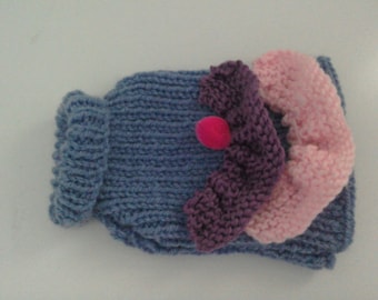 Puede incluir: Un suéter de punto azul con un adorno de flor rosa y morada. La flor tiene un pompón rosa en el centro.