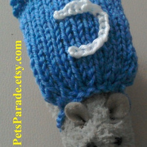 May include: A blue knitted hat with a white letter C on it. The hat is on top of a grey stuffed animal with a long snout.