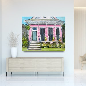 Puede incluir: Una pintura de una casa rosa con un porche blanco y plantas verdes en frente. La casa tiene una puerta azul y ventanas blancas. La pintura est&aacute; hecha en un estilo suelto e impresionista.