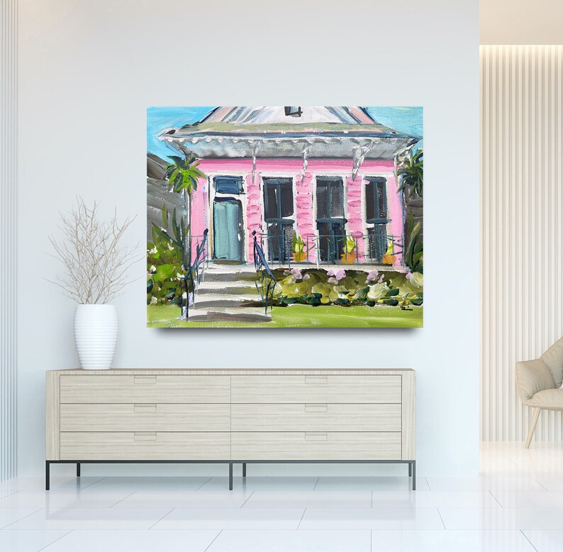 Puede incluir: Una pintura de una casa rosa con un porche blanco y plantas verdes en frente. La casa tiene una puerta azul y ventanas blancas. La pintura est&aacute; hecha en un estilo suelto e impresionista.