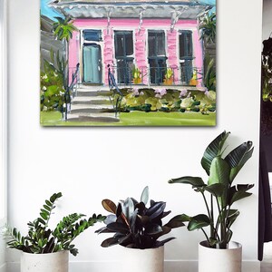 Puede incluir: Una pintura de una casa rosa con un techo blanco y un c&eacute;sped verde. La casa tiene una puerta azul y ventanas blancas. Hay plantas en macetas en el porche.