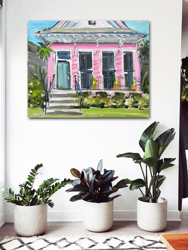Puede incluir: Una pintura de una casa rosa con un techo blanco y un c&eacute;sped verde. La casa tiene una puerta azul y ventanas blancas. Hay plantas en macetas en el porche.