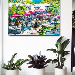 May include: A colorful painting of an outdoor cafe scene with pink umbrellas, white tables and chairs, and a fountain in the background.