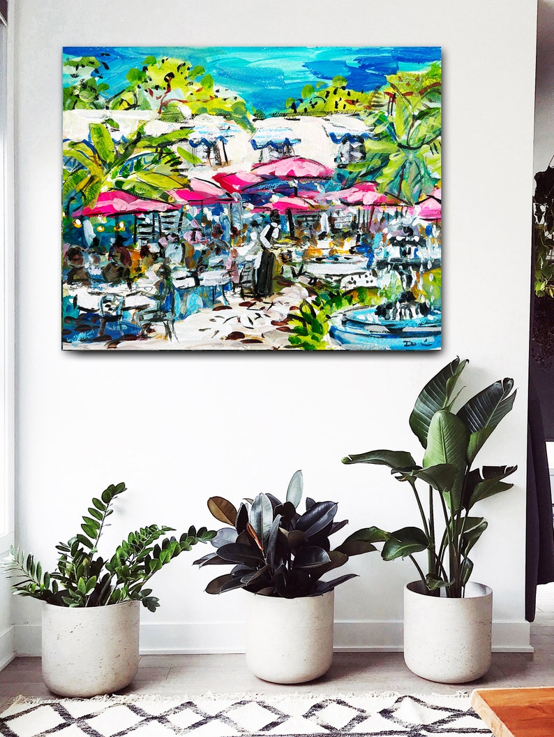 May include: A colorful painting of an outdoor cafe scene with pink umbrellas, white tables and chairs, and a fountain in the background.