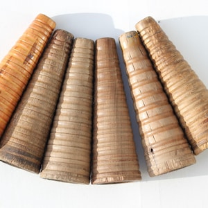 May include: A collection of six vintage wooden textile cones arranged in a fan shape. Each cone features a tapered, ribbed cylindrical body with varying shades of natural wood grain, ranging from light tan to darker brown, showing signs of wear.