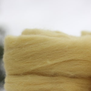 May include: A close-up of a pile of light yellow wool roving. The wool is soft and fluffy, and it is perfect for felting or spinning.
