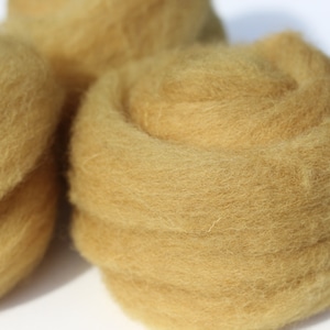 Könnte beinhalten: Nahaufnahme eines Stapels goldgelber Wollrohlinge. Die Wolle ist weich und flauschig und perfekt zum Filzen oder Spinnen.