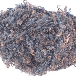Könnte beinhalten: Ein Knäuel dunkelgrauer und brauner lockiger Wolle. Die Wolle ist aus Wolle und eignet sich perfekt zum Stricken oder Häkeln.