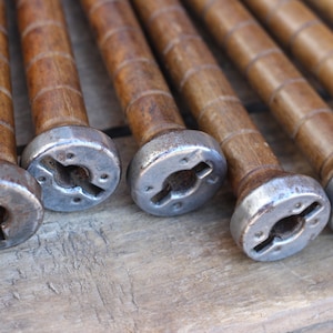 May include: Close-up of eight wooden spools with metal caps. The spools are brown and have a grooved texture. The metal caps are silver and have a keyhole-shaped opening.