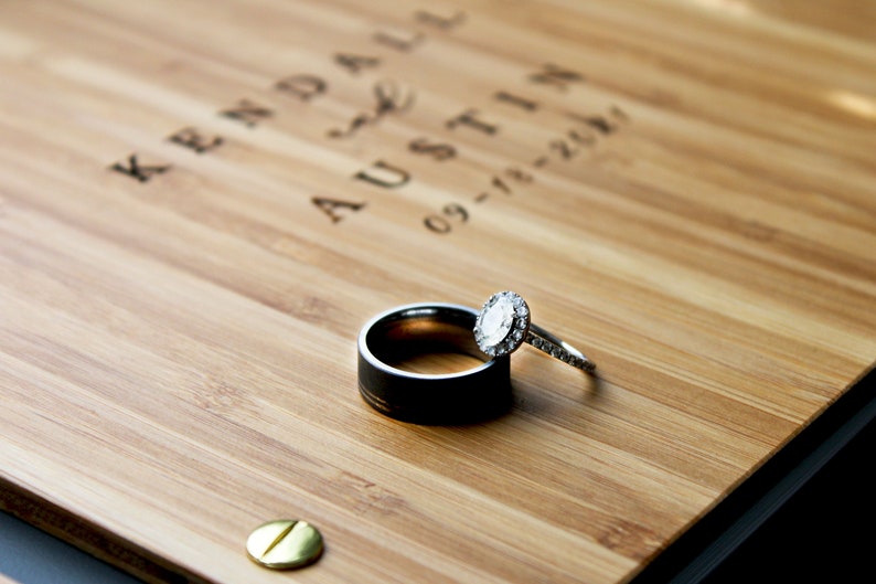 Close-up of a couple's wedding rings resting on the cover of their custom wooden guest book.
