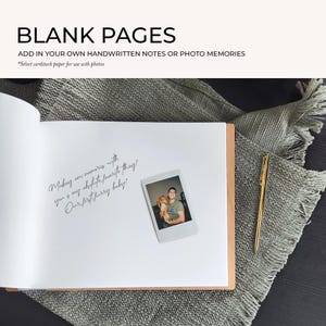 a blank book with a handwritten note and a small Polaroid photo of a couple, along with a pen and a gray blanket on a wooden surface.