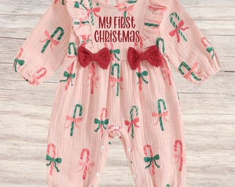 Könnte beinhalten: Hellrosa Baby-Strampler mit langen Ärmeln und rundem Ausschnitt. Der Strampler ist mit Zuckerstangen- und Schleifenmustern in Grün und Rot verziert. Der Text "MY FIRST CHRISTMAS" ist auf der Vorderseite aufgedruckt, darunter zwei rote Schleifen.