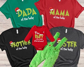 May include: A set of five Christmas-themed t-shirts for a family. The shirts are green, red, black, and gray with the text "Dada of the baby", "Mama of the baby", "Brother of the baby", "The Baby who stole Christmas!" and "Sister of the baby".