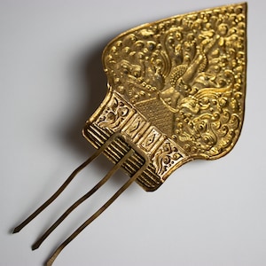 以下が含まれることがあります： 金色の装飾的なヘアコーム。葉の形をした詳細なデザイン。櫛は、人物や模様の複雑な彫刻が施されており、ベースから伸びる3つの長い歯があります。 全体的な美しさはアンティークで装飾的です。