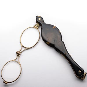Op de afbeelding: Een vintage tortoiseshell vouwbril met goudkleurige metalen accenten. De bril heeft twee ronde glazen en een scharnierend handvat.