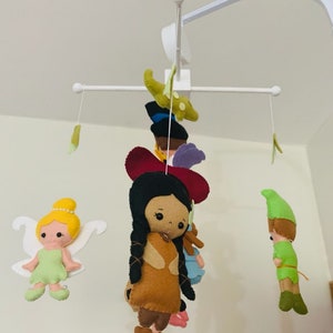 Pu&ograve; includere: Un mobile bianco per neonati con personaggi in feltro appesi. I personaggi includono Peter Pan, Trilly, Pocahontas e un alligatore verde. Il mobile &egrave; progettato per la cameretta di un bambino.