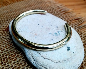 May include: A simple gold-toned metal bangle bracelet. The bracelet is smooth and has a rounded shape.