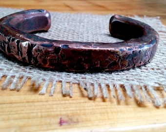 May include: A hammered copper bracelet with a rustic, aged finish. The bracelet is thick and has a rounded shape.