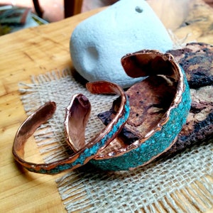 May include: Two copper bracelets with turquoise inlay. The bracelets are stacked on top of each other and have a rustic, handmade look.