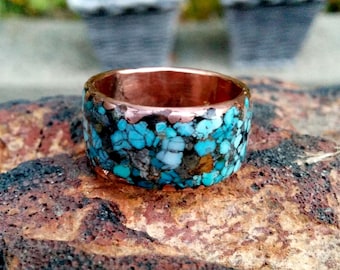 May include: A copper ring with a wide band, inlaid with turquoise and other stones. The ring has a rustic, handcrafted look.